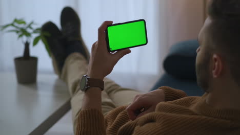 Mann-Hält-Smartphone-Horizontal-Und-Sieht-Sich-Videos-An,-Die-Zu-Hause-Oder-Im-Büro-Ruhen,-Greenscreen-Technologie-Für-Die-Montage-Moderner-Geräte-Und-Anwendungen